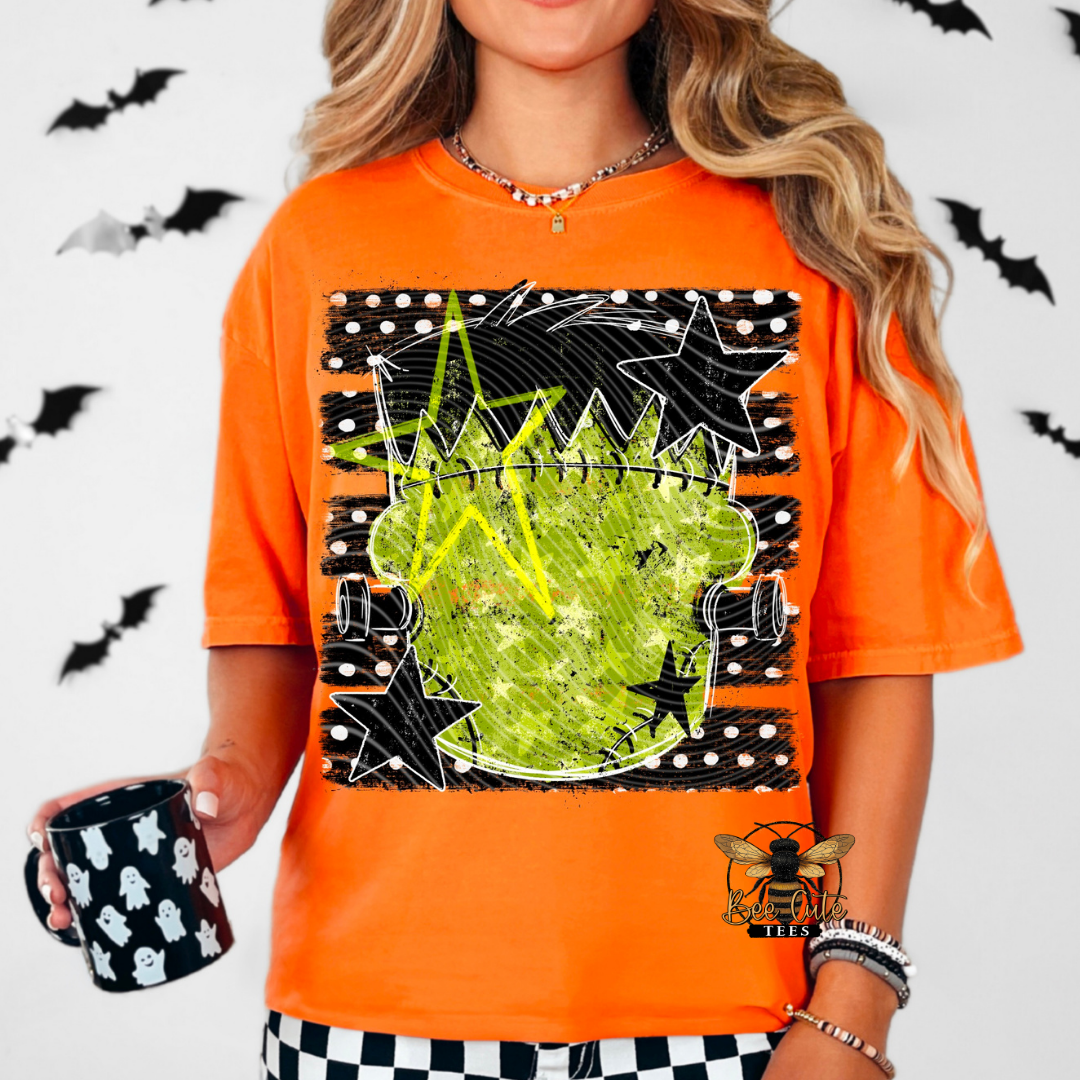 A woman wearing a bright orange graphic t-shirt with a Halloween-themed design featuring a green pumpkin, black stars, and bats. She is holding a black mug with white ghosts, set against a white background decorated with black bats.