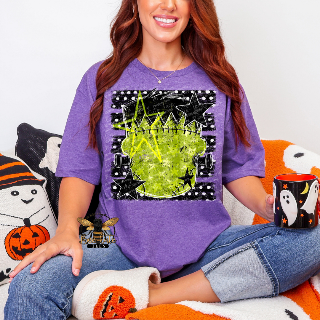 A woman wearing a purple graphic t-shirt with a green cauldron and black stars design, sitting on an orange and white couch and holding a black mug with a ghost pattern.