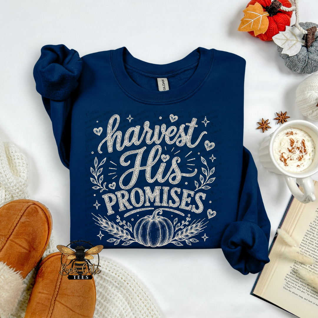 A navy blue long-sleeve t-shirt with a white graphic reading 'harvest His PROMISES' and a pumpkin design, styled in a cozy flat-lay with autumn props including a mug of coffee, an open book, and brown shoes.