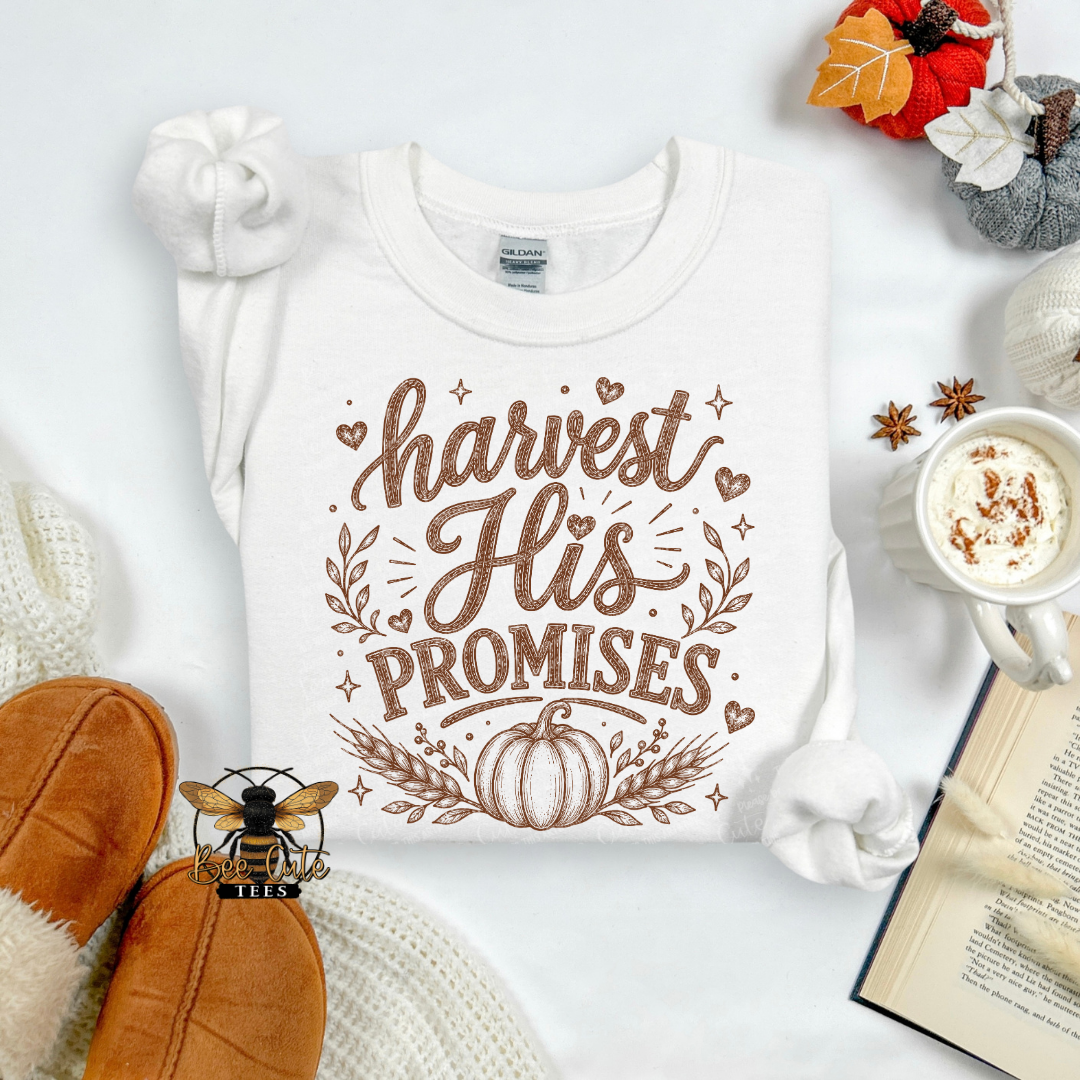 A white long-sleeve t-shirt with a brown graphic reading 'harvest His PROMISES' and a pumpkin design, styled in an autumn flat lay with slippers, a mug of coffee, an open book, and fall leaves.