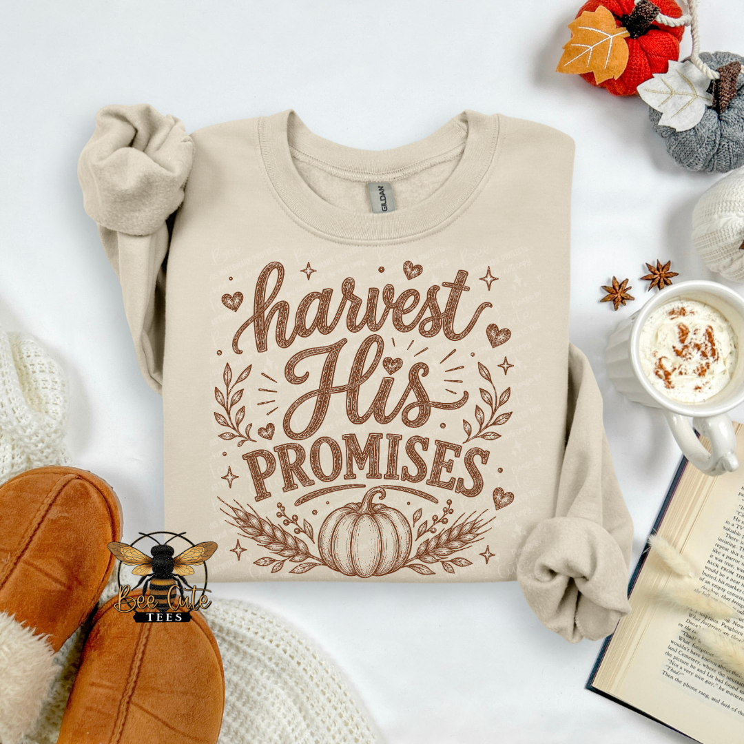 A beige long-sleeve crewneck sweatshirt with a brown graphic reading 'harvest His PROMISES' and a pumpkin design, styled in a cozy flat lay with orange slippers, a mug of coffee, an open book, and autumn decorations.