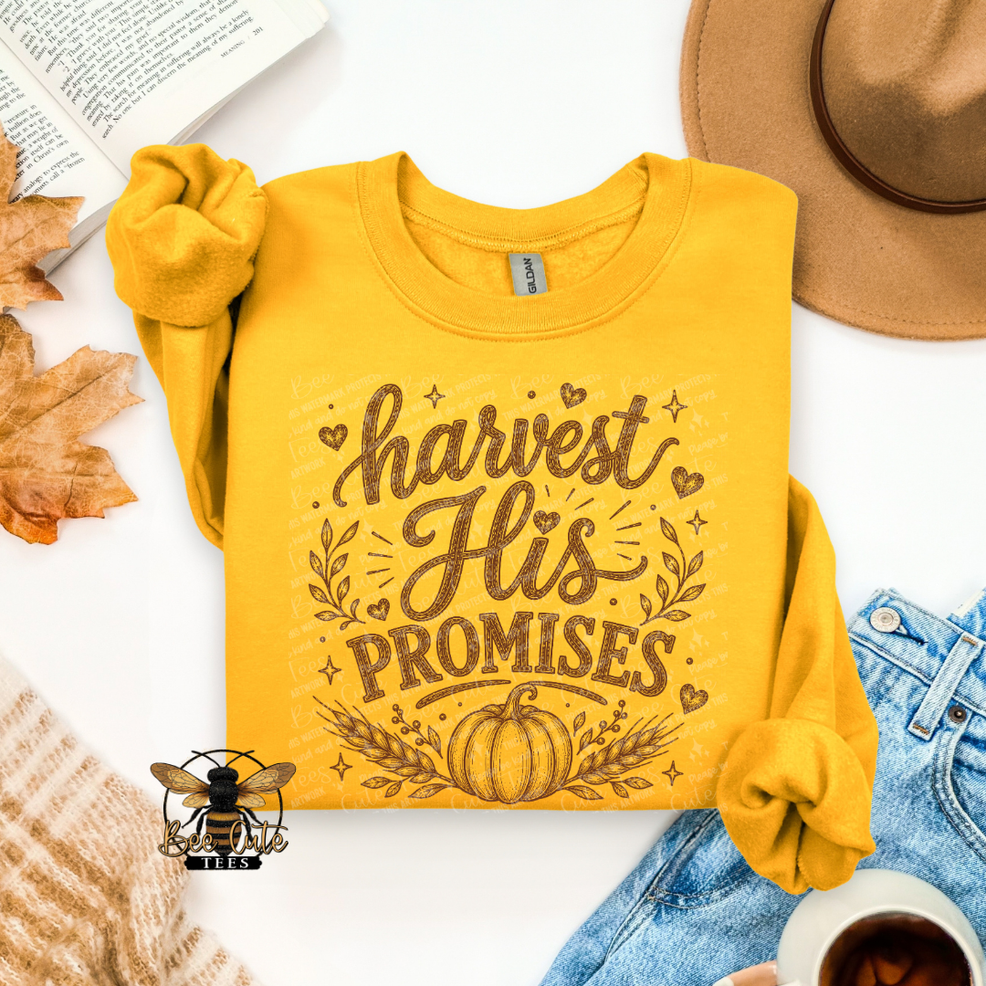 A folded yellow long-sleeve sweatshirt with rolled cuffs, featuring a brown graphic that reads 'harvest His PROMISES' with a pumpkin and leaf design. The sweatshirt is styled in a flat lay with a tan hat, blue jeans, a book, autumn leaves, a cup of coffee, and a small bee logo watermark.