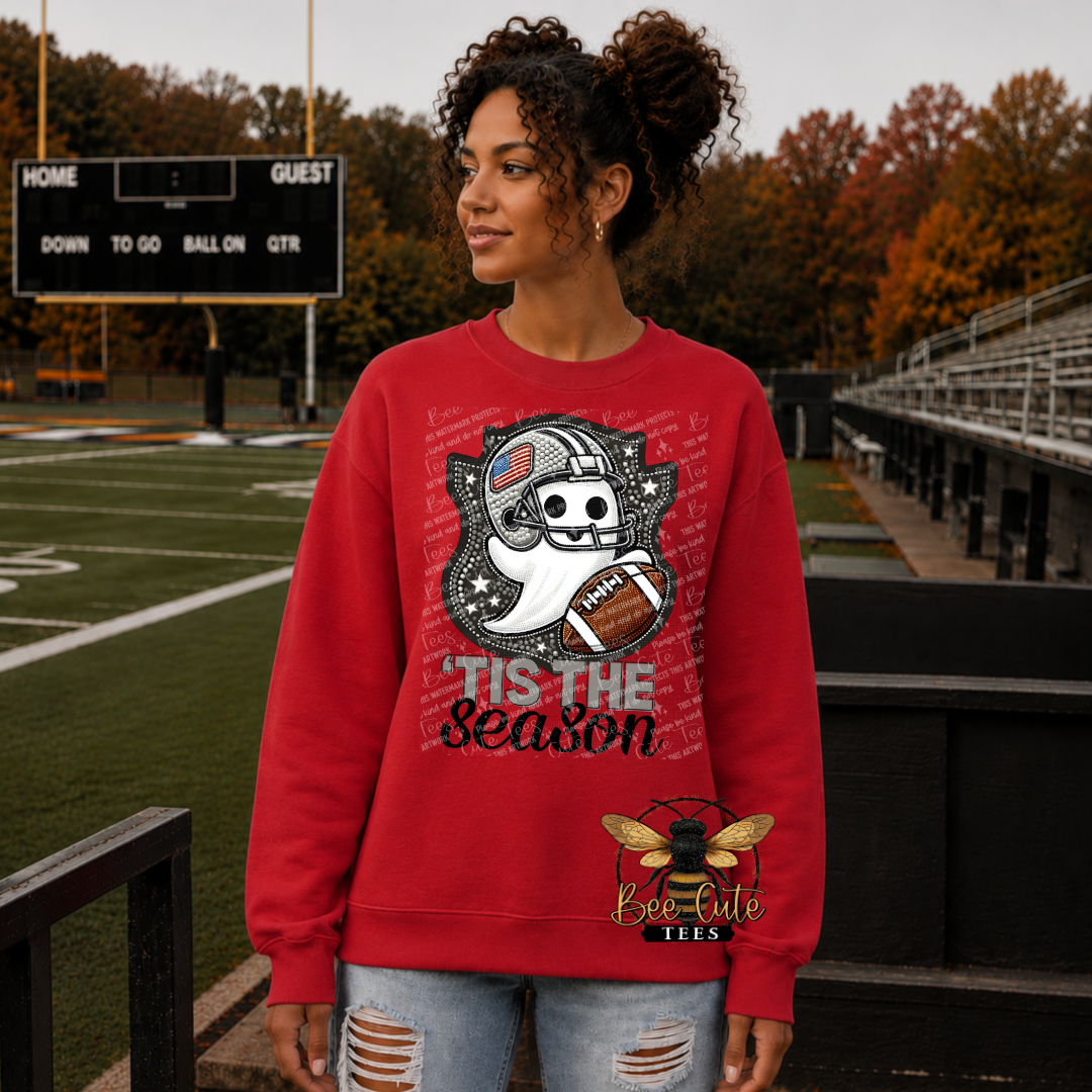 A woman wearing a red crewneck sweatshirt with a cartoon ghost football graphic and the text 'Tis the Season' on a football field background.