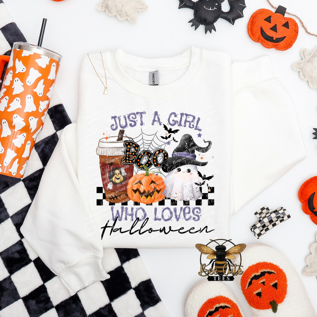 An white crewneck sweatshirt with a Halloween-themed graphic print reading 'JUST A GIRL WHO LOVES Halloween' in text, featuring jack-o'-lanterns, a ghost, bats, and a witch hat. The sweatshirt is styled in a flat-lay arrangement with a black and white checkered blanket, a ghost-patterned tumbler, and other spooky props on a white background.