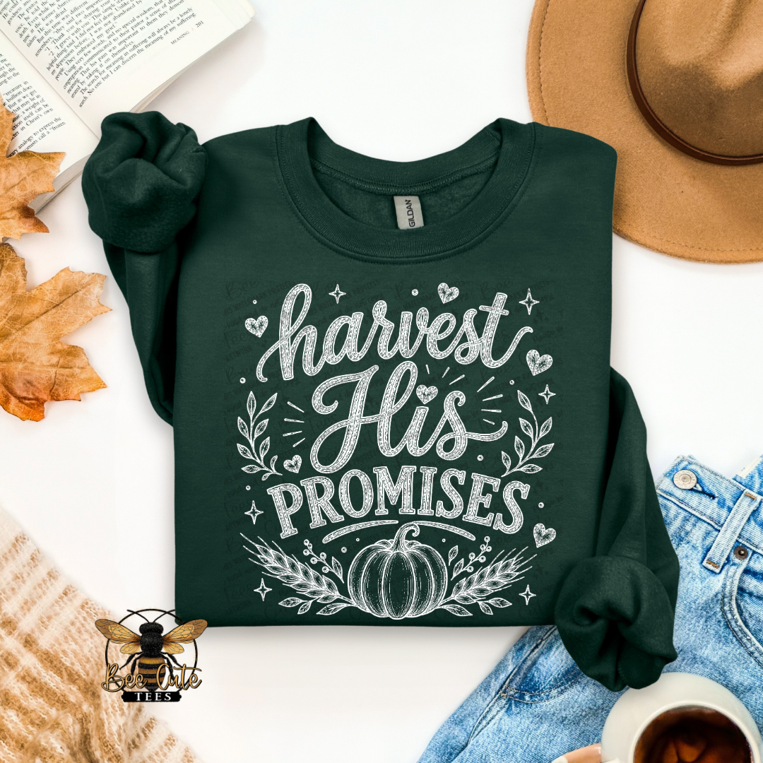 A dark forest green long-sleeve t-shirt with a white graphic print reading 'harvest His PROMISES' with a pumpkin and leaf design, styled in a flat lay with a tan hat, blue jeans, a book, autumn leaves, a cup of coffee, and a knit sweater.