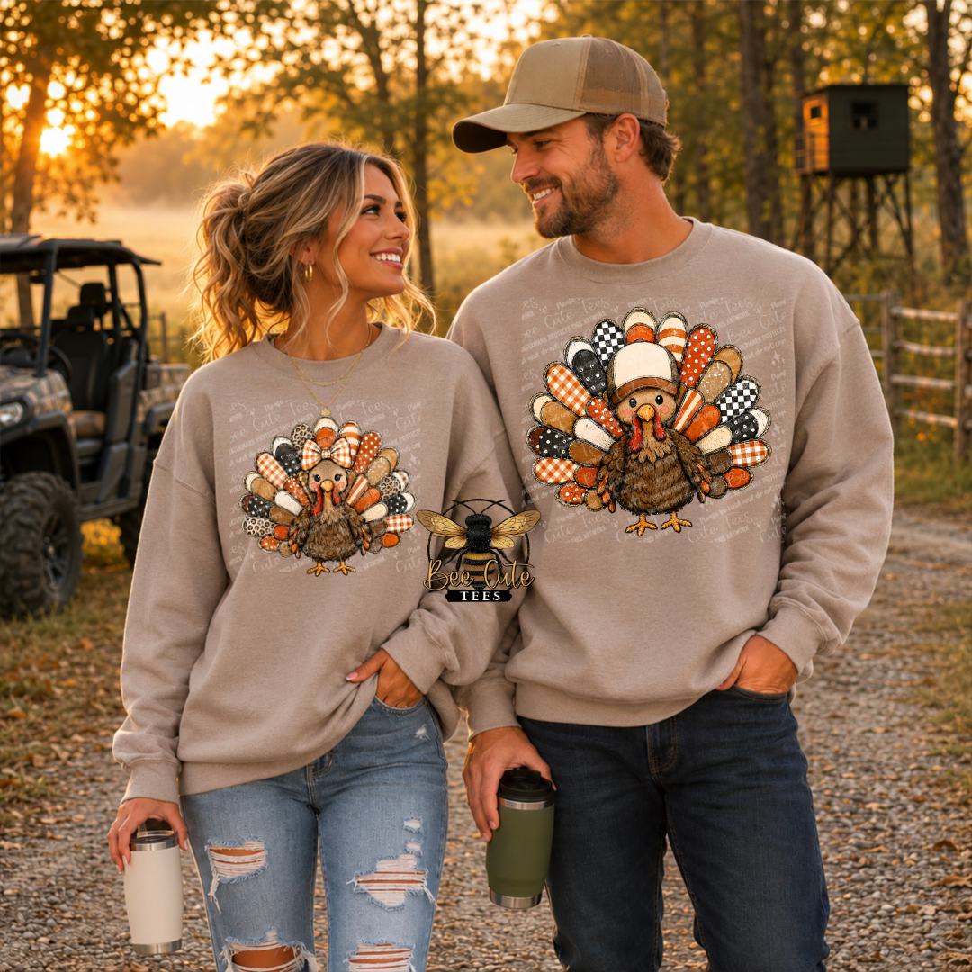 A man and a woman standing outdoors in a wooded setting at sunset, both wearing matching beige crewneck sweatshirts with a large colorful turkey graphic on the front. 