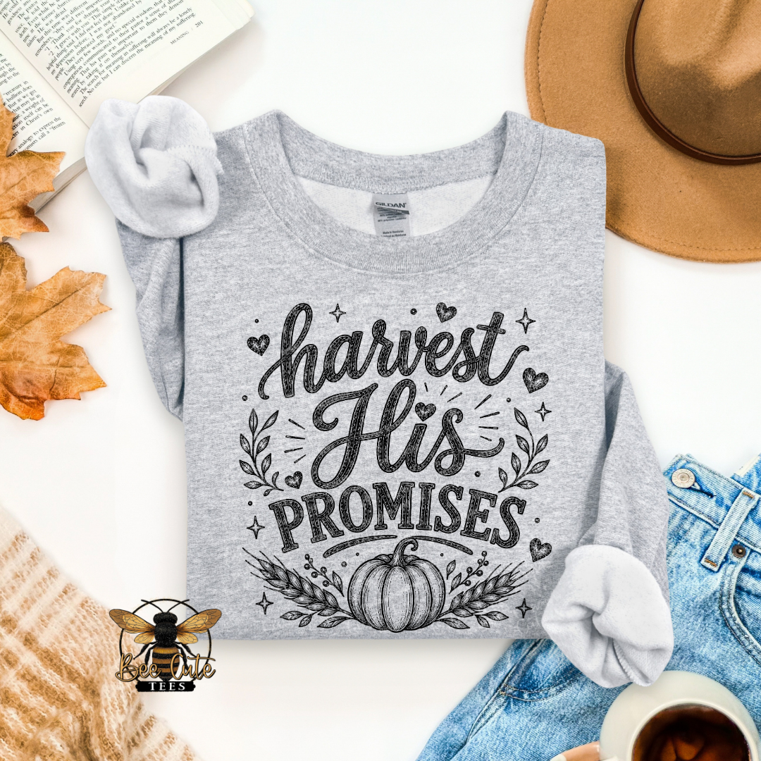 A heather gray long-sleeve t-shirt with a black graphic reading 'harvest His PROMISES' and a pumpkin design, styled in a flat lay with a tan hat, blue jeans, a book, autumn leaves, a cup of coffee, and a knit sweater.