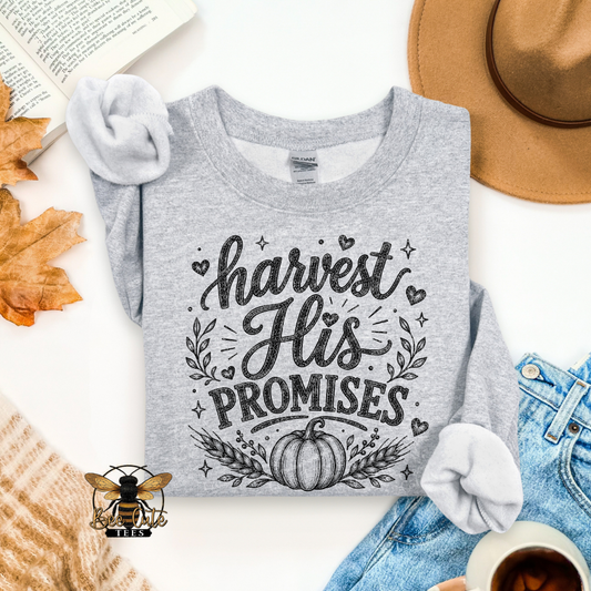 A heather gray long-sleeve t-shirt with a black graphic reading 'harvest His PROMISES' and a pumpkin design, styled in a flat lay with a tan hat, blue jeans, a book, autumn leaves, a cup of coffee, and a knit sweater.