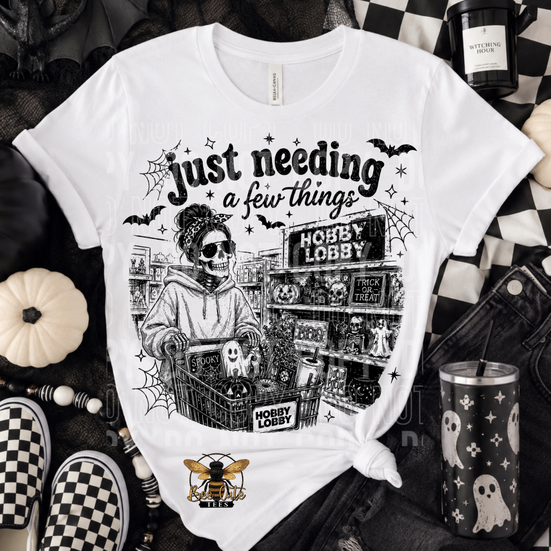 A white graphic t-shirt featuring a black and white illustration of a skeleton shopper in a Halloween-themed store, styled in a flat-lay with dark denim, checkered shoes, a pumpkin, and a tumbler.