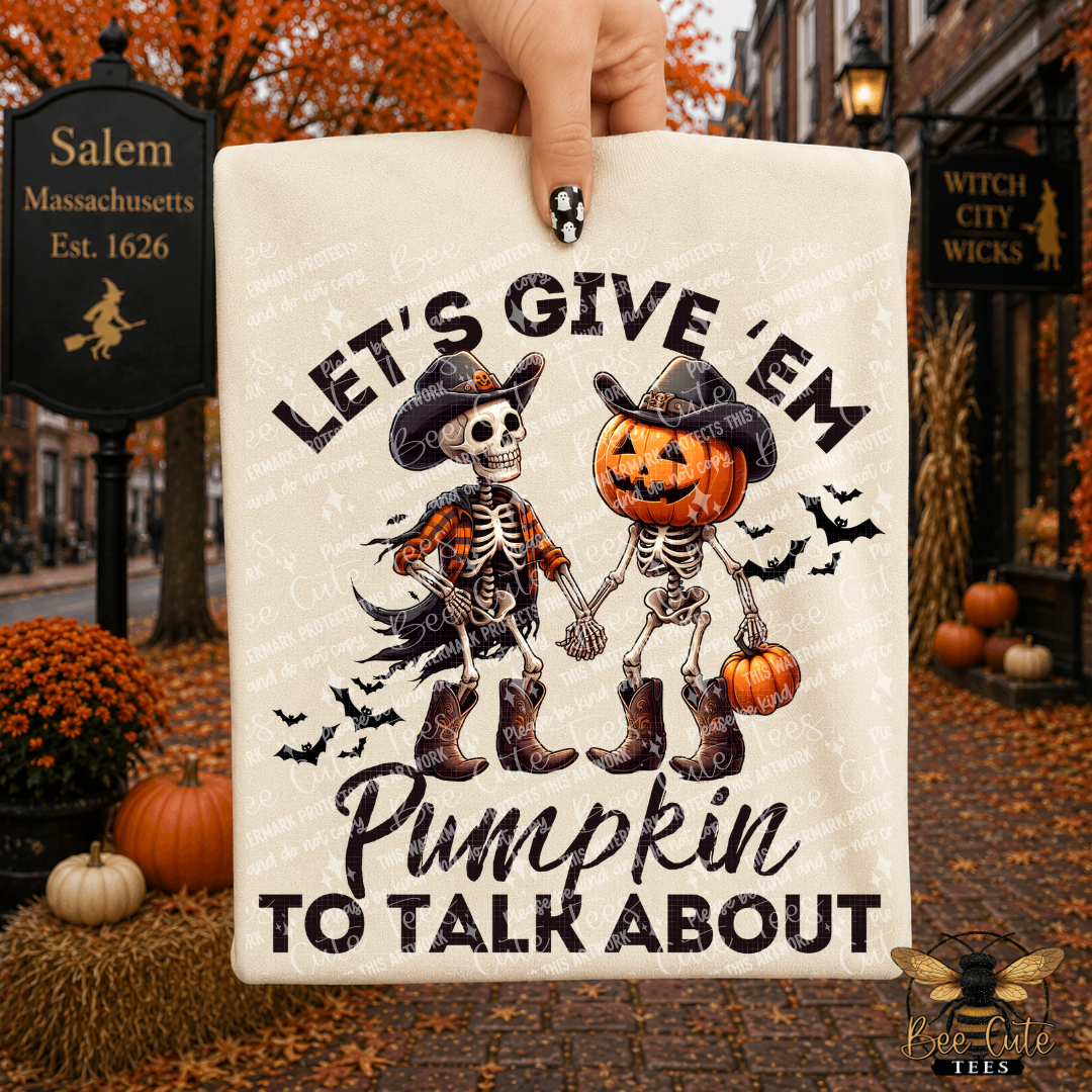 A hand holds a cream-colored t-shirt featuring a Halloween graphic of two skeletons holding hands, one as a pirate and one as a pumpkin-headed character. The text reads 'LET'S GIVE 'EM Pumpkin TO TALK ABOUT'.