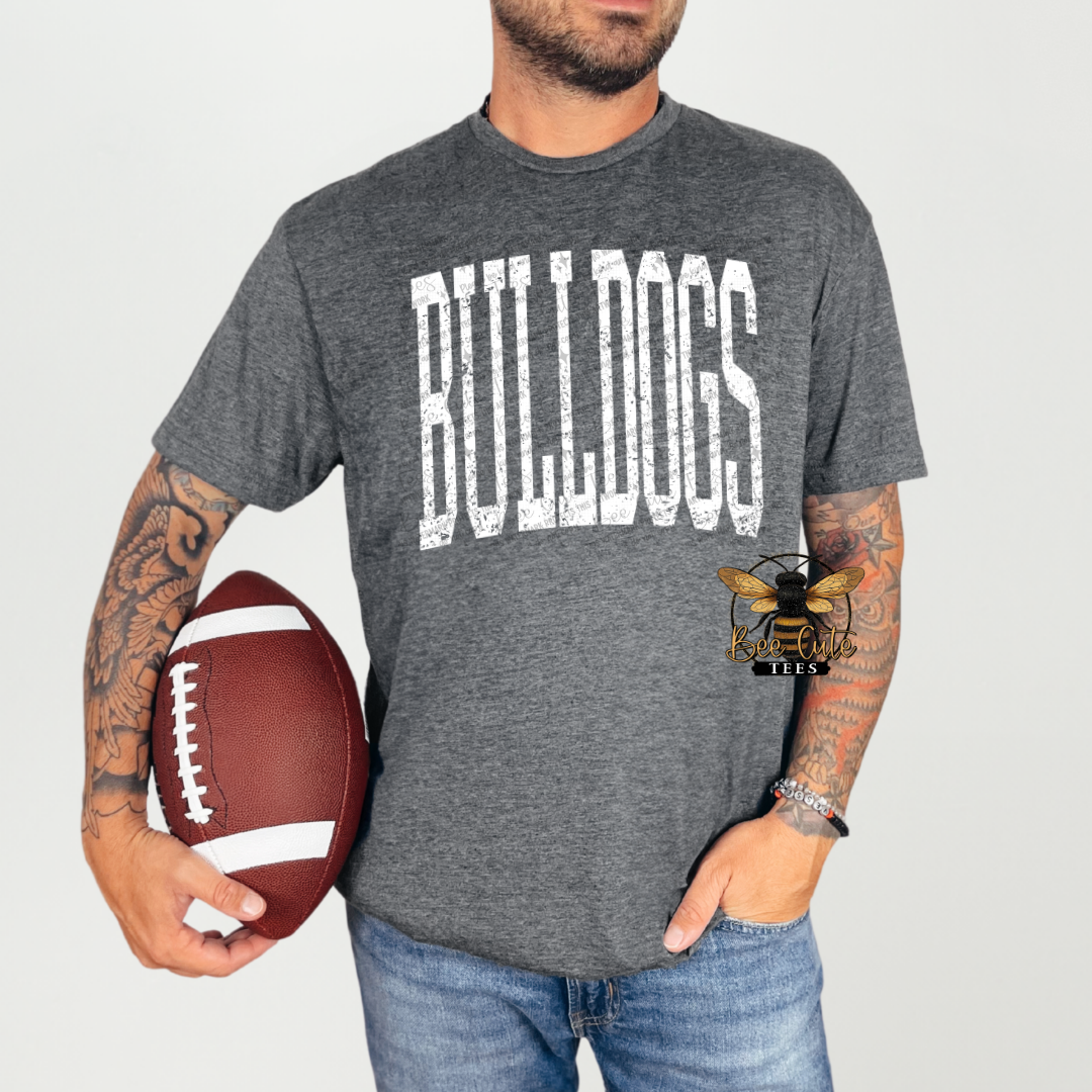 A man wearing a heather gray t-shirt with 'BULLDOGS' printed in distressed white block letters, holding a brown football against a light gray background.