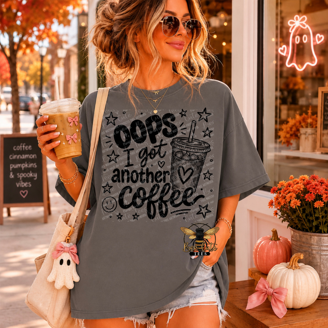 A woman wearing a gray graphic t-shirt with the text 'OOPS I got another Coffee' and a coffee cup illustration, holding a coffee cup and wearing a ghost charm bag in a cozy autumn storefront setting.