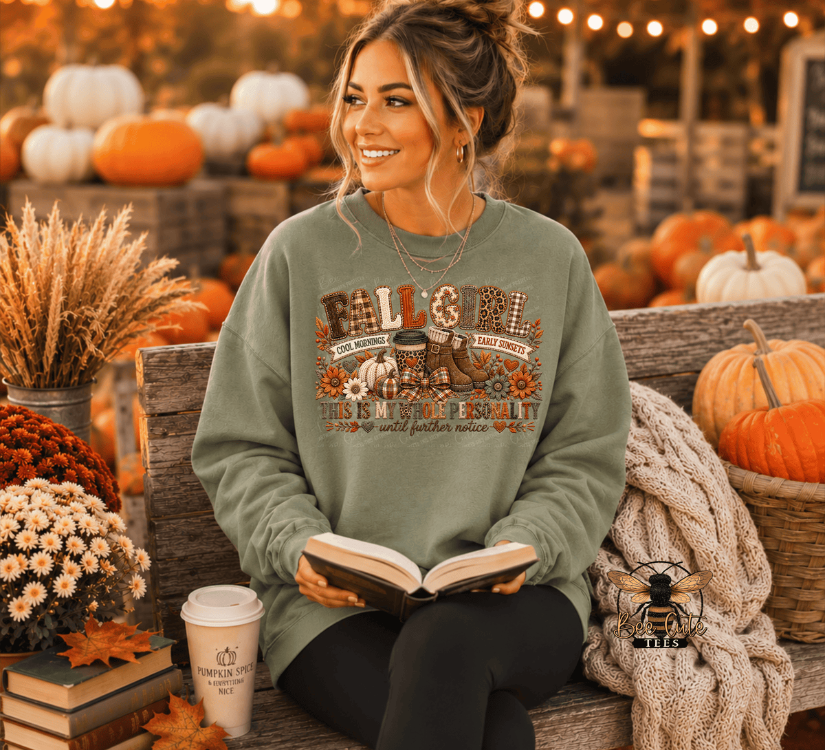 A woman sitting on a wooden bench in an autumn-themed setting, wearing an olive green crewneck sweatshirt with a 'Fall Gossip' graphic. She is holding an open book, with a coffee cup, a knit blanket, and pumpkins in the background.
