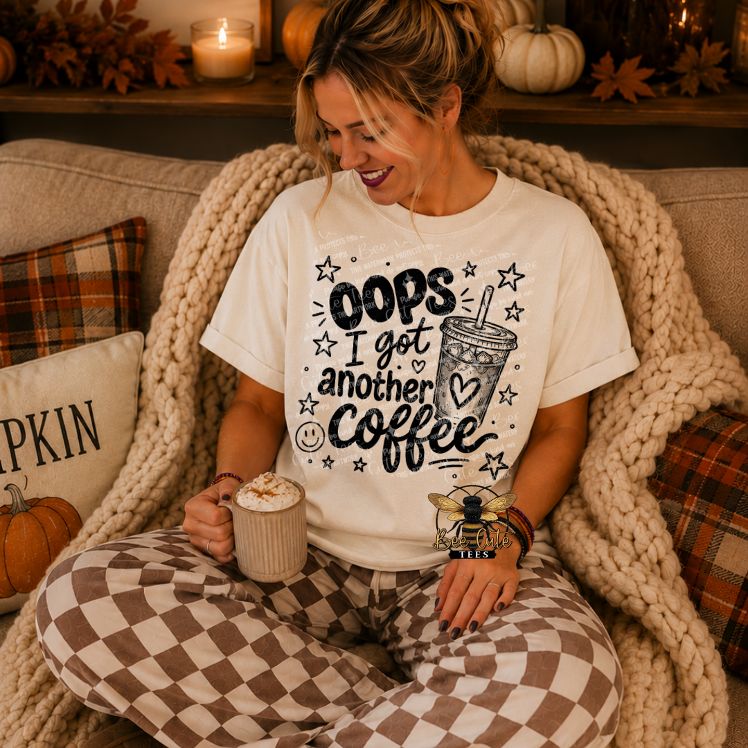 A woman sitting on a couch wrapped in a chunky knit blanket, wearing a white graphic t-shirt that reads 'OOPS I get another coffee' with a coffee cup illustration, and brown-and-white checkered pajama pants.