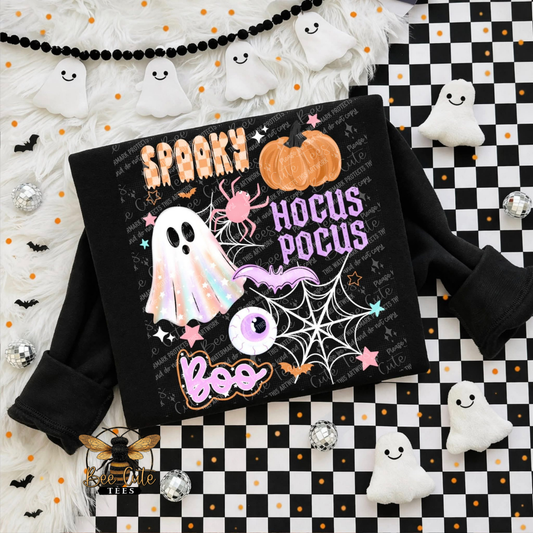 A black long-sleeve sweatshirt featuring a colorful Halloween graphic with the words 'Spooky Hocus Pocus Boo' and illustrations of a ghost, pumpkin, spider, bat, and eye, styled in a flat lay on a black-and-white checkered surface with white ghost decorations.