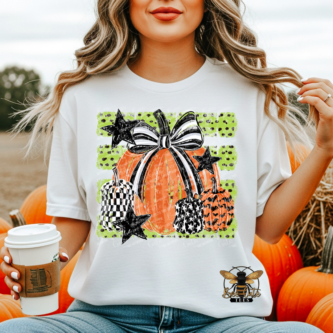 A woman wearing a white graphic t-shirt with a Halloween pumpkin design, sitting among pumpkins in an outdoor setting.