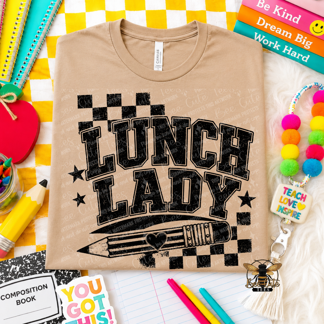 A beige short-sleeve t-shirt with a black distressed graphic reading 'LUNCH LADY' above a pencil illustration, styled in a flat lay with school supplies and colorful accessories.
