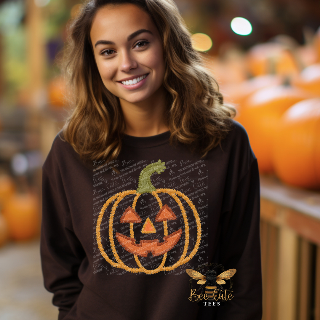 A smiling woman wearing a dark brown crewneck sweatshirt with a pumpkin graphic, posed in front of a blurred background of pumpkins. The sweatshirt features a jack-o'-lantern design with orange and yellow details, and a Bee-Cute Tees logo is visible in the bottom right corner.