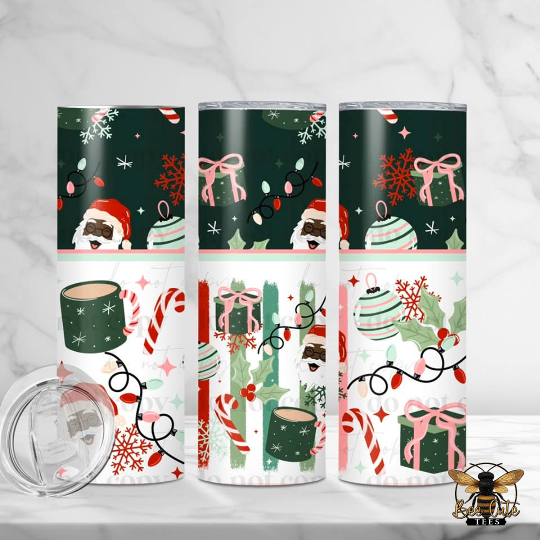 Three tall insulated tumblers with a Christmas-themed wrap design are displayed on a light marble surface, with a clear lid shown in the lower left. The design features Santa Claus, gift boxes, candy canes, snowflakes, and holiday lights on dark green and white sections.