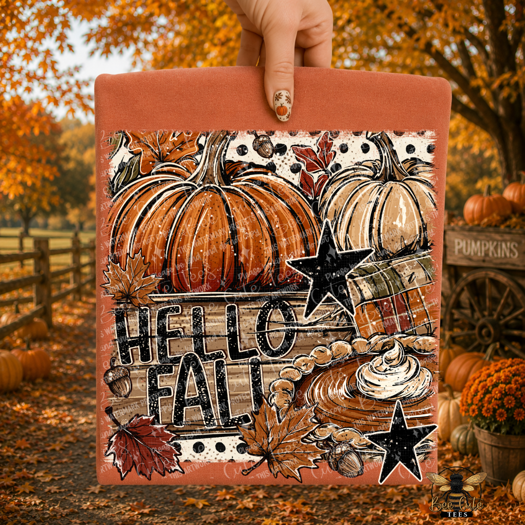 A hand holds a folded orange t-shirt featuring a fall-themed graphic with pumpkins, autumn leaves, stars, and the words “HELLO FALL.” The background shows an outdoor autumn scene with orange trees, pumpkins, and fall foliage.