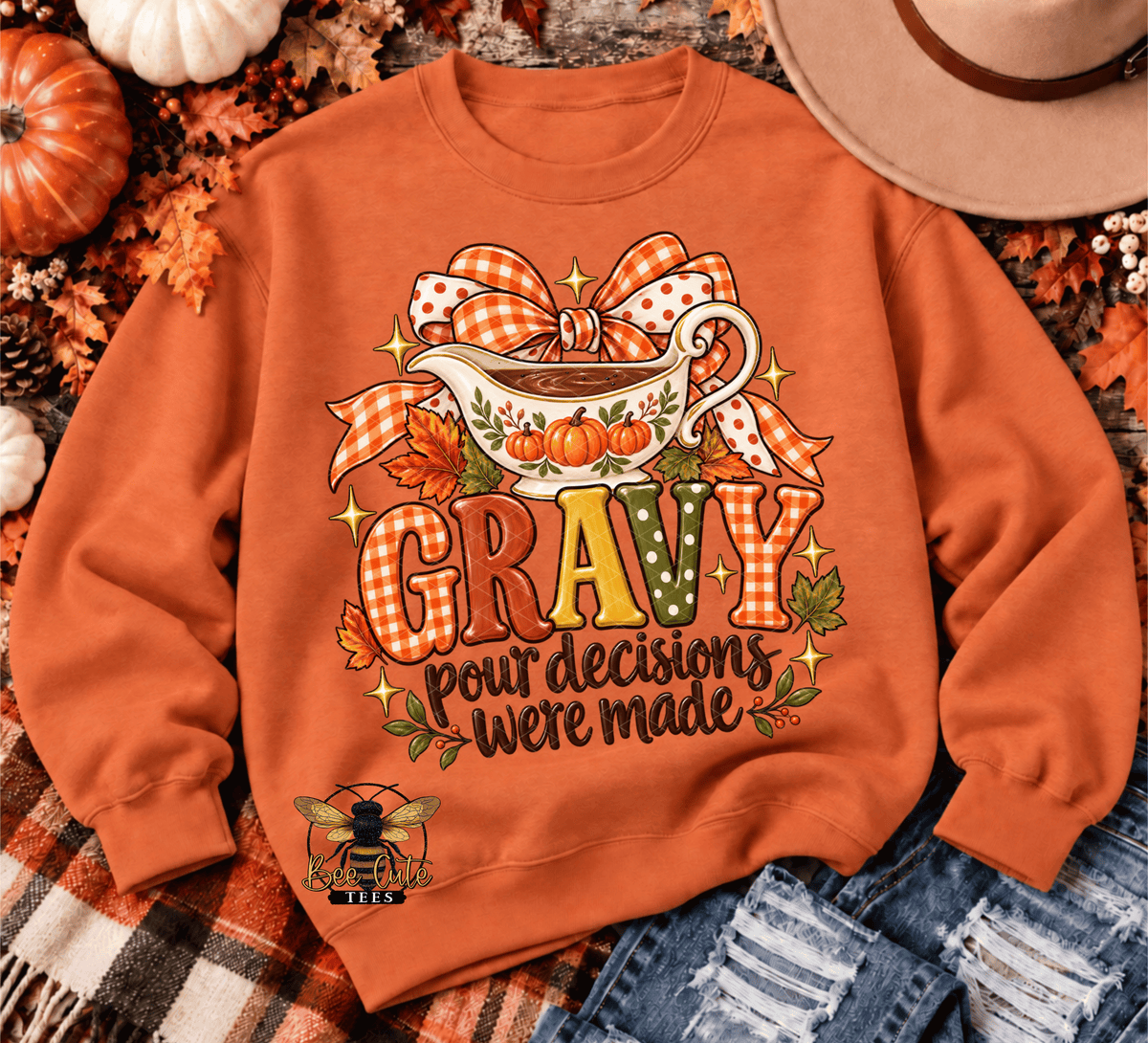 An orange crewneck sweatshirt with a fall-themed 'Gravy' graphic, styled in a flat lay with autumn leaves, pumpkins, a cowboy hat, and denim jeans.