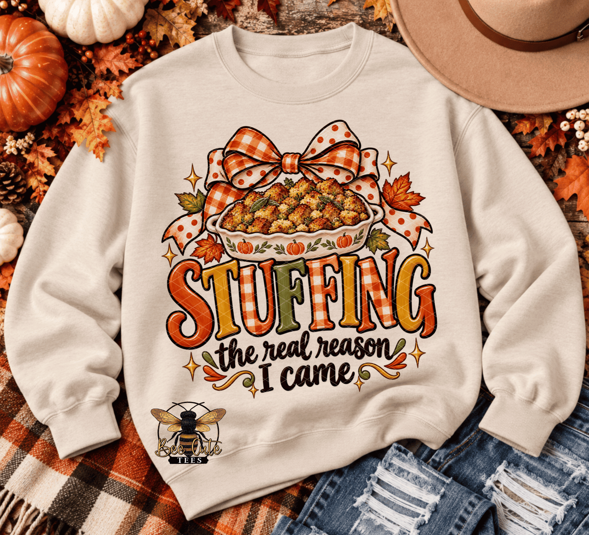 A cream-colored crewneck sweatshirt with a Thanksgiving-themed graphic that reads 'STUFFING the real reason I came' in orange, yellow, and green lettering. The graphic features a bowl of stuffing under a plaid bow.