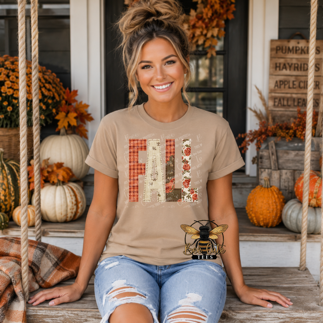 A woman sitting on a porch swing wearing a beige graphic t-shirt with 'FALL' spelled out in autumn-themed patchwork letters, paired with distressed blue jeans.