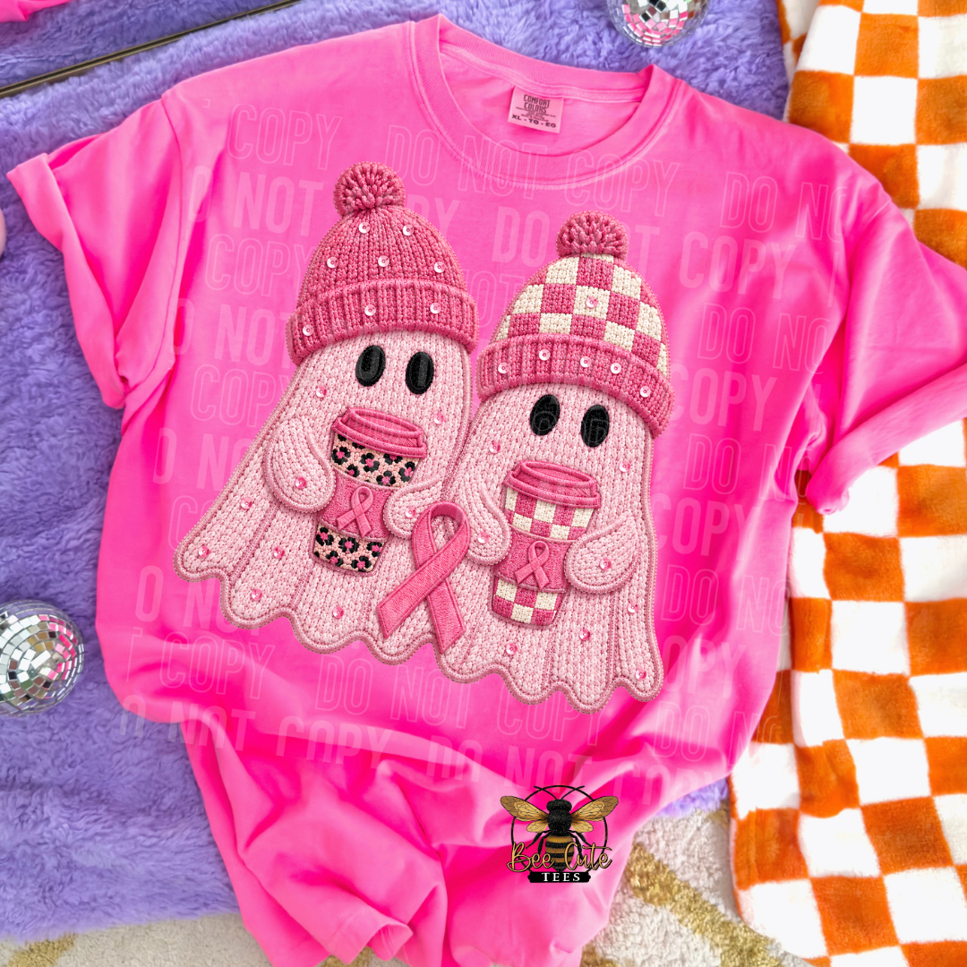 A bright pink short-sleeve t-shirt featuring a graphic of two cute pink knit ghosts holding pink awareness ribbons. The ghosts are decorated with pink and white checkered and leopard-print knit hats.