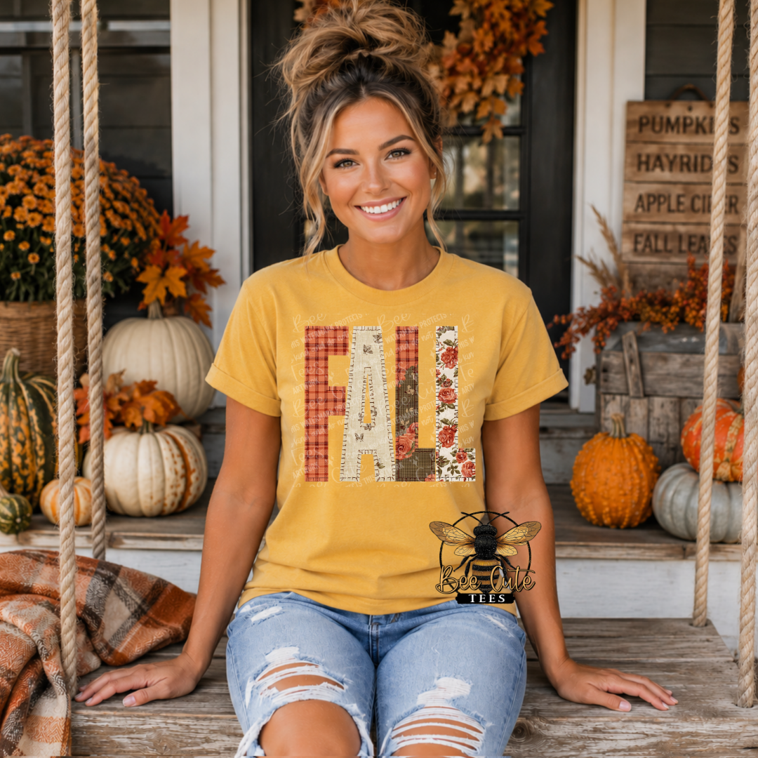 A woman sitting on a porch wearing a mustard yellow graphic t-shirt with the word 'FALL' made of autumn-themed patches. The background is decorated with pumpkins, fall leaves, and rustic signs.