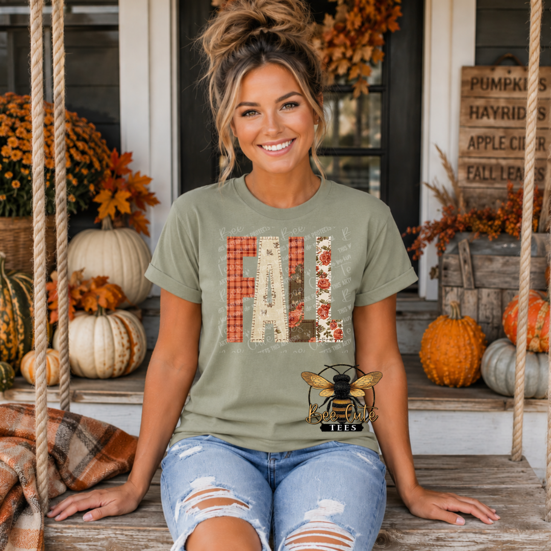 A woman sitting on a porch swing wearing an olive green graphic t-shirt with 'FALL' in plaid and floral patterns, paired with distressed denim jeans. The background is decorated with pumpkins, autumn leaves, and a rustic wooden sign.