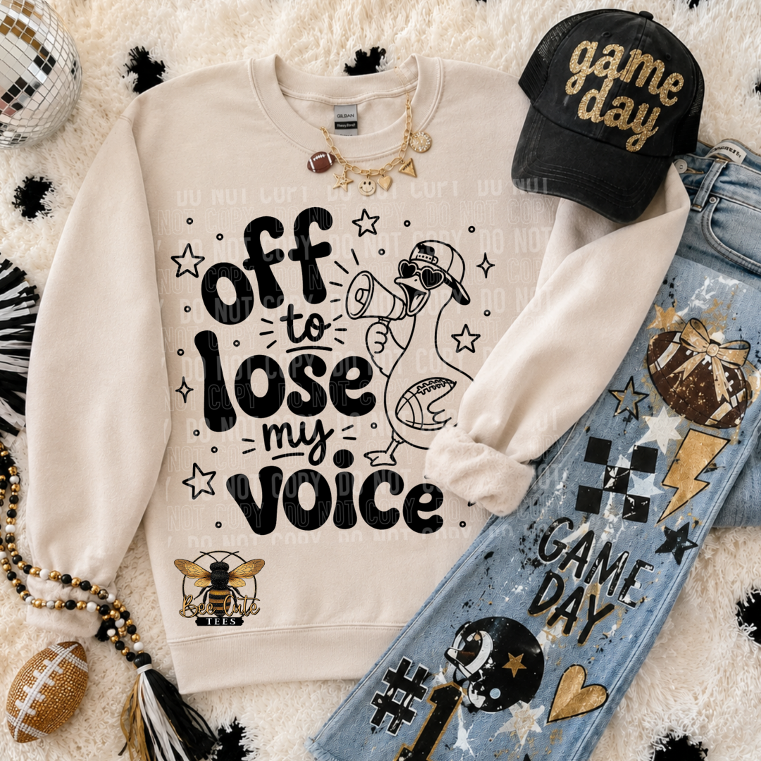 A styled flat-lay featuring a cream sweatshirt with the text 'off to lose my voice' and a duck graphic, arranged with a black 'game day' cap, blue jeans, a football, and accessories on a white faux-fur background.