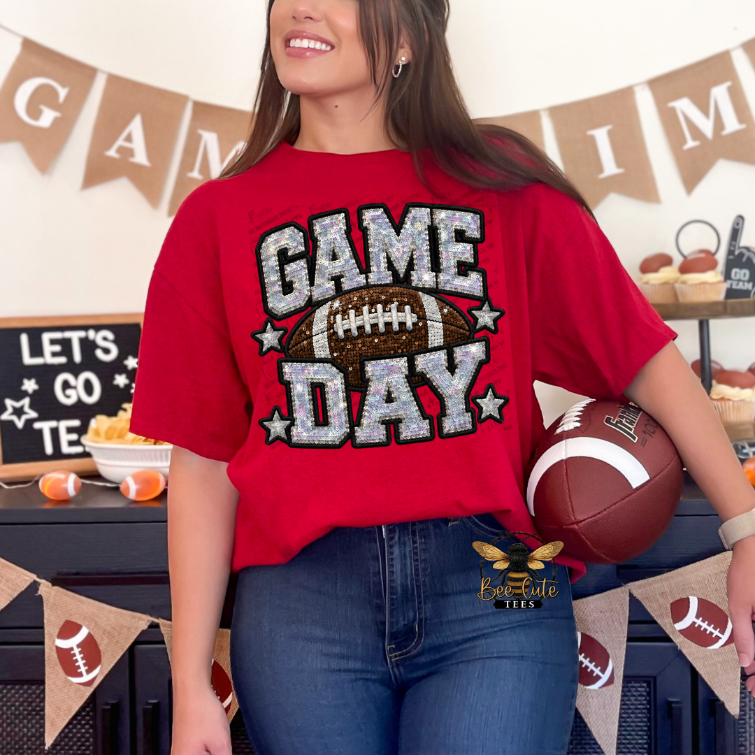 A woman wearing a red graphic t-shirt with a glittery 'GAME DAY' design and a football, holding a football in a decorated party setting.