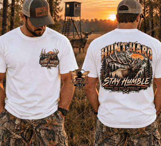 Two men shown from the front and back wearing matching white graphic t-shirts and camouflage hunting pants, standing in a wooded field at sunset with a deer stand and deer in the background. The front shirt has a small chest graphic, and the back shirt has a large moose graphic with the words 'HUNT HARD' and 'STAY HUMBLE'.