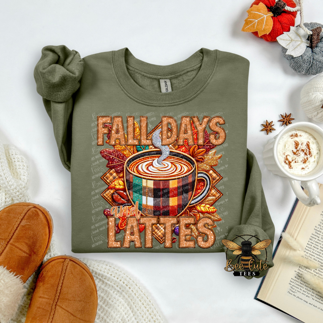 An olive green long-sleeve t-shirt with a 'Fall Days Lattes' graphic, styled in a cozy flat-lay arrangement with a mug of coffee, a book, knit socks, and autumn-themed decorations.