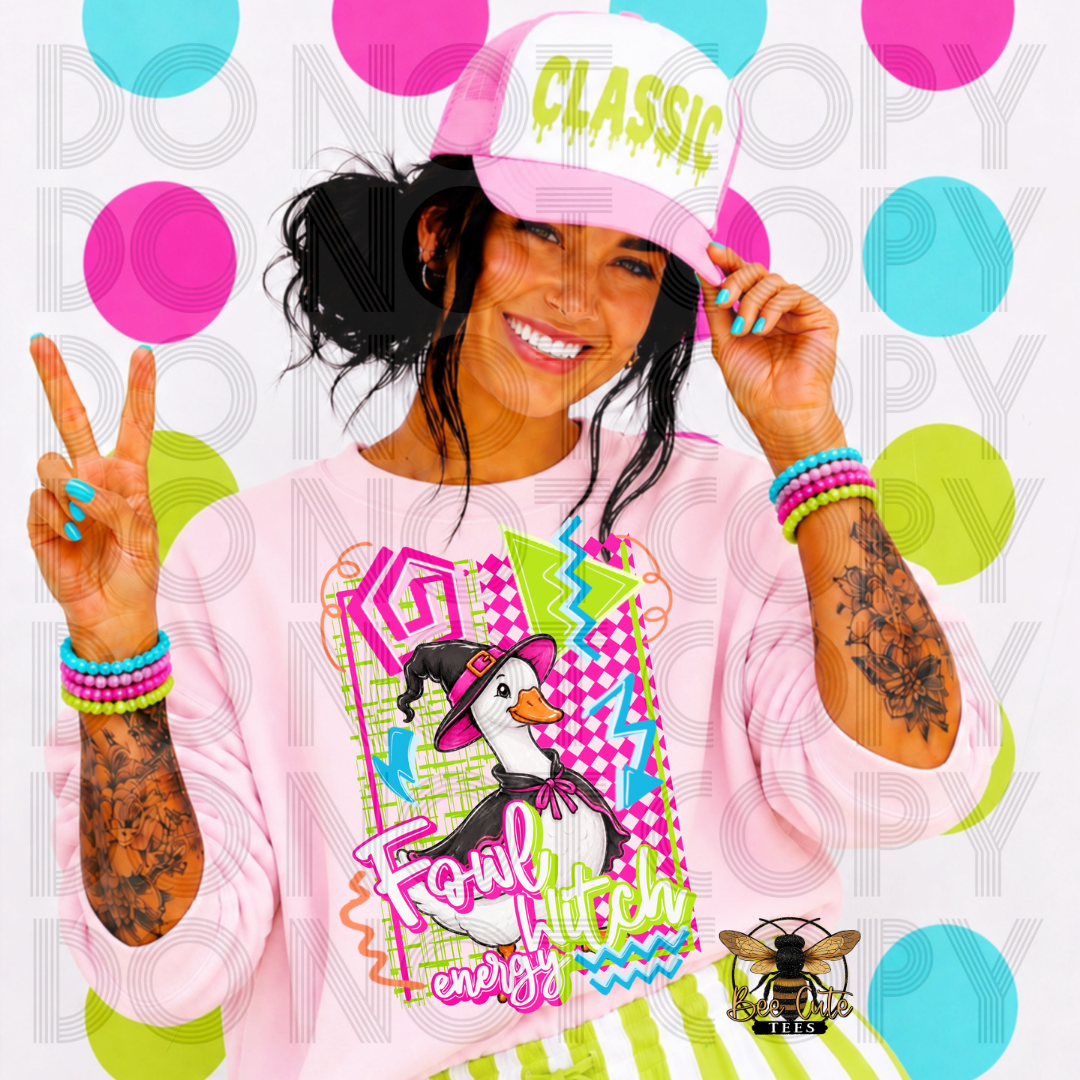 A woman wearing a pink long-sleeve graphic sweatshirt and a pink cap with the word 'CLASSIC' in green, posing against a white background with colorful pink, blue, and green polka dots. The sweatshirt features a graphic of a penguin in a witch hat with the text 'Fowl Witch energy'.