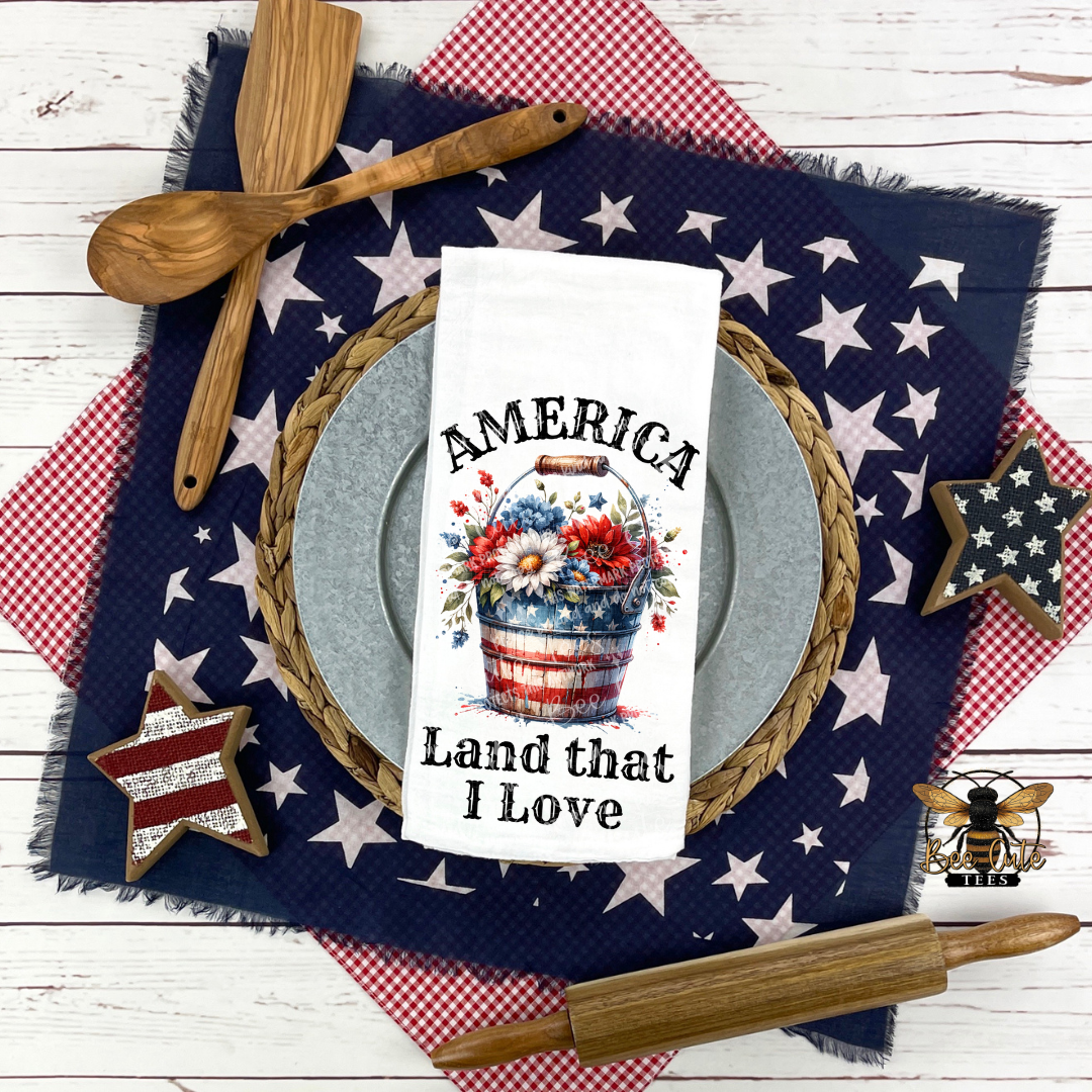 Decorative table setting with 'America Land that I Love' towel, wooden spoon, and rolling pin on a star-patterned cloth.