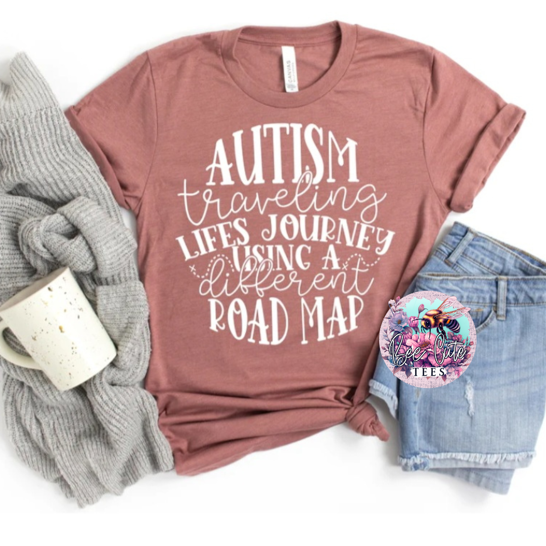 A casual outfit setup with a brown crewneck sweatshirt featuring the text 'AUTISM traveling life's journey using a different road map' in white. The setup includes a pair of blue denim jeans and a grey knit sweater, presented on a white background.