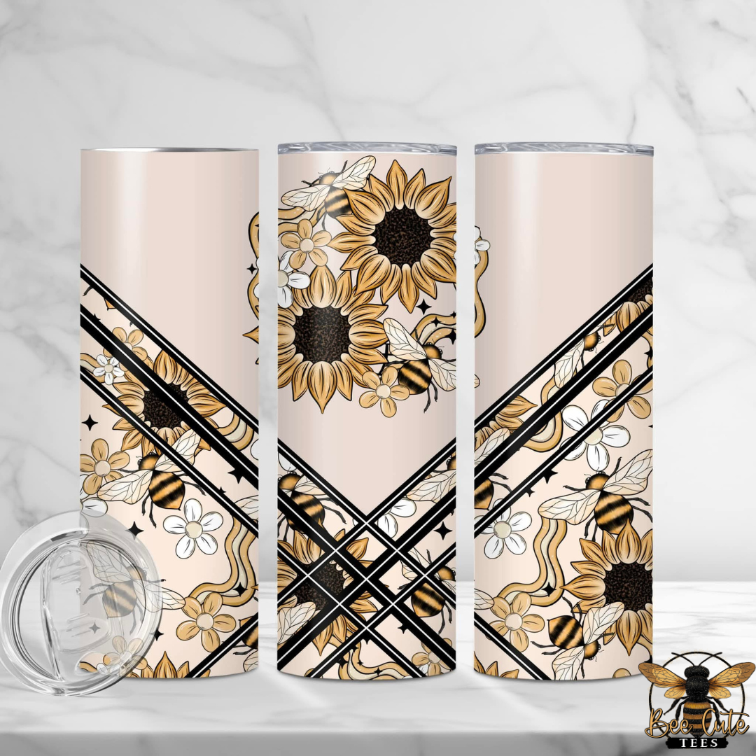 Three tall insulated tumblers with a floral and bee pattern on a pale blush background, shown on a white marble surface with a clear lid in the foreground. A small bee logo with 'TEES' appears in the bottom right corner.