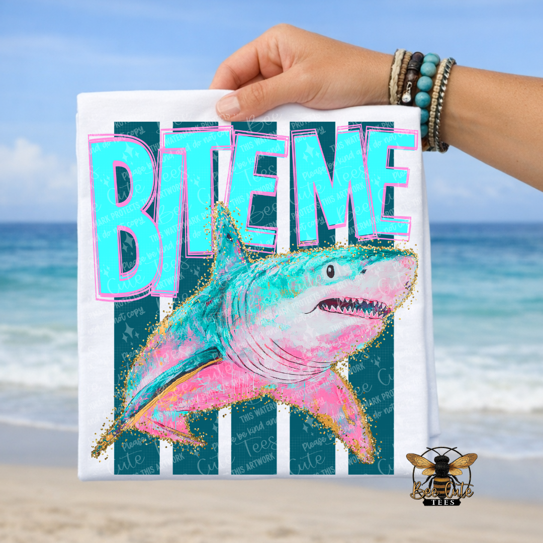 White t-shirt with a shark design and 'BITE ME' text held by a hand on a beach background