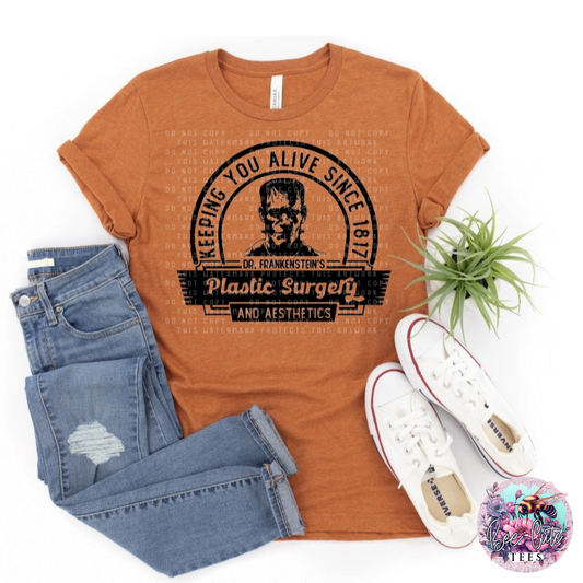 An orange t-shirt with text and a graphic related to plastic surgery, displayed flat with a pair of blue jeans, a white sneaker, and a potted plant.