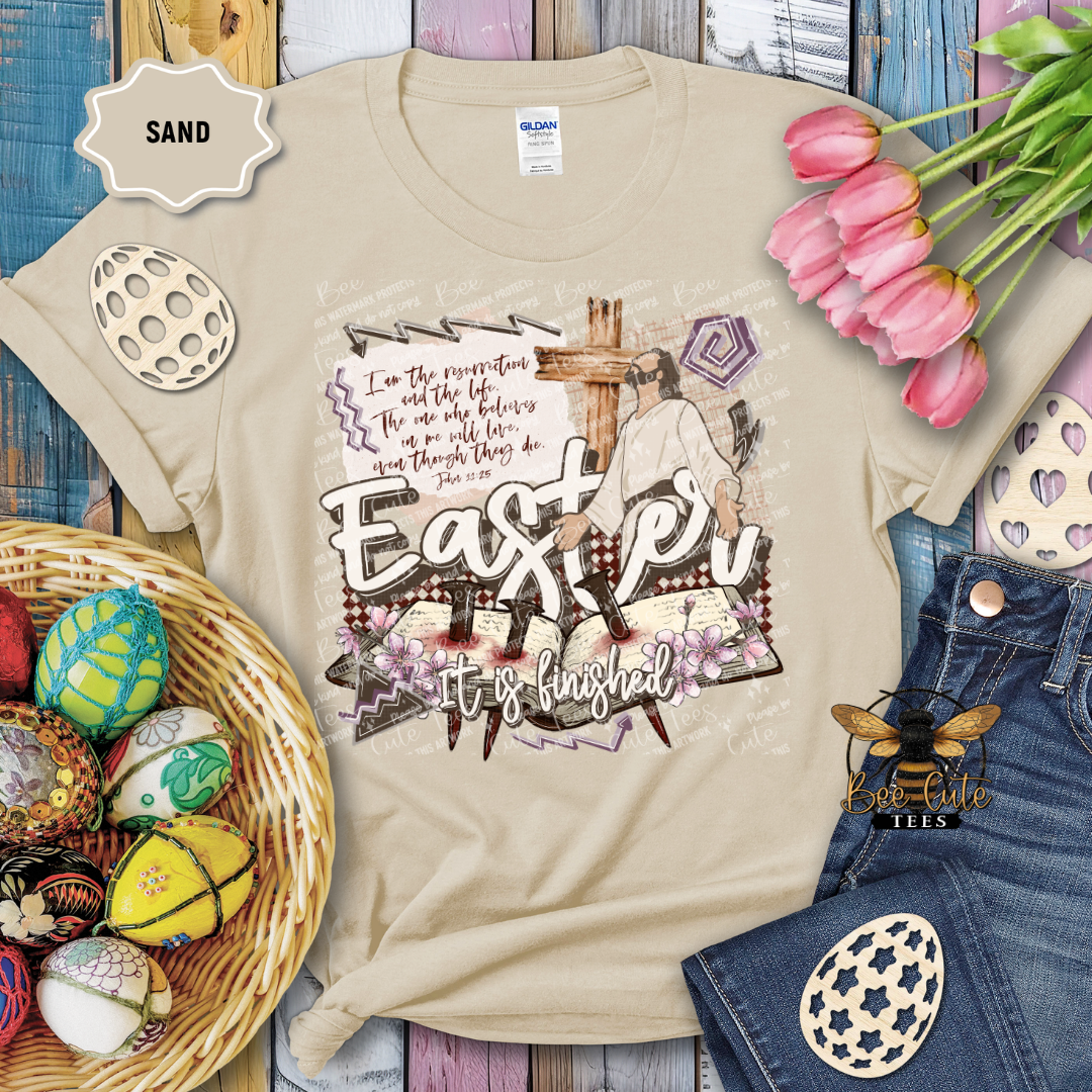 Beige t-shirt with Easter design featuring a cross and text, surrounded by Easter decorations on a wooden surface.