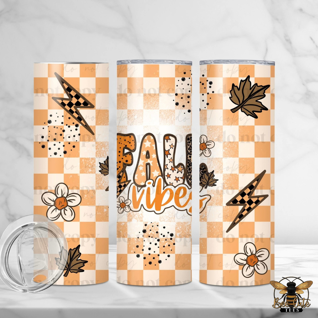 Three views of a 20 oz skinny tumbler with a fall-themed design, featuring a checkered orange and white pattern, lightning bolts, maple leaves, flowers, and the text 'Fall Vibes'. A clear lid is shown in the bottom left corner on a white marble background.