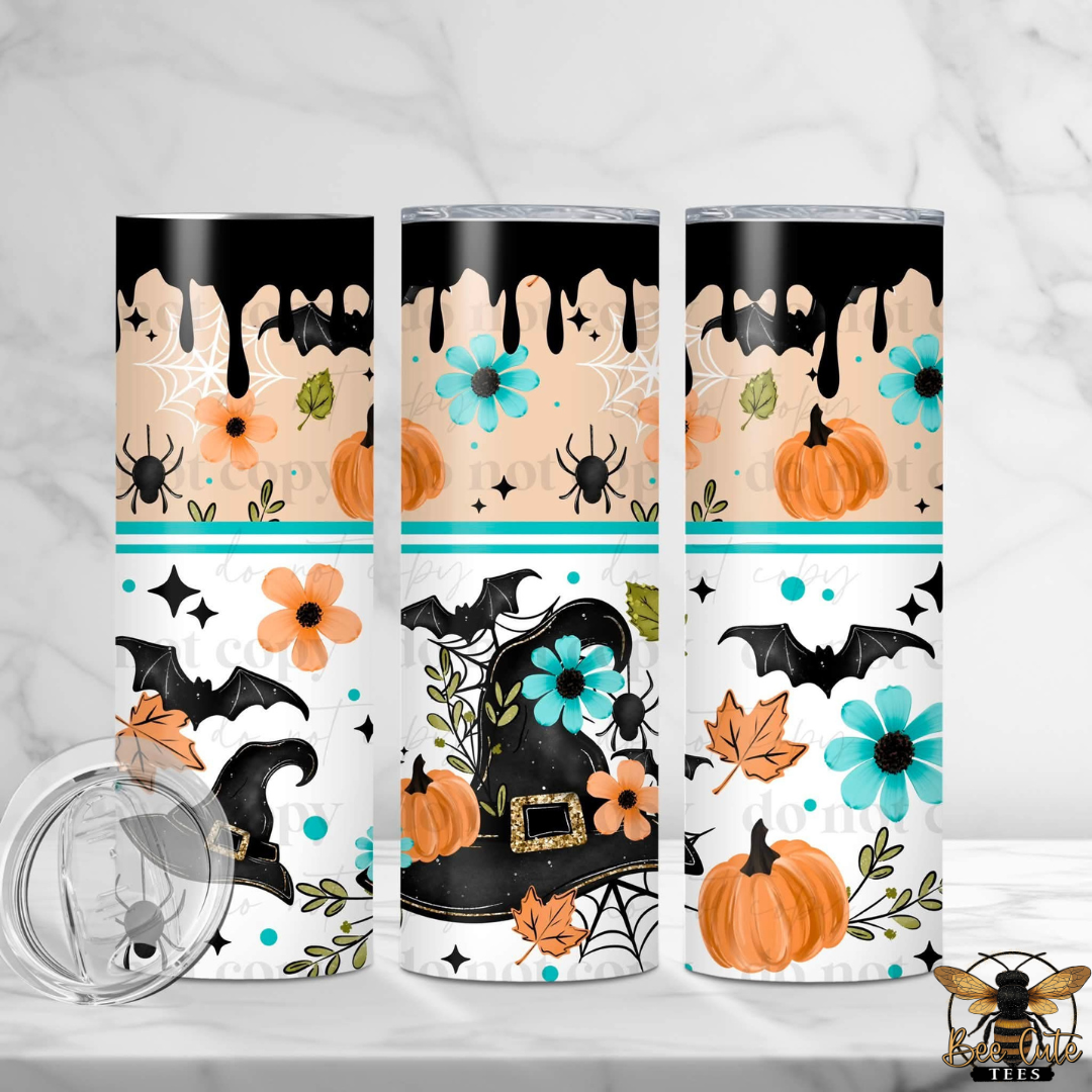 Three tall insulated tumblers with a Halloween-themed wrap design are displayed on a white marble surface. The design features black dripping paint, orange pumpkins, black bats, orange and blue flowers, spiders, and a witch's hat.