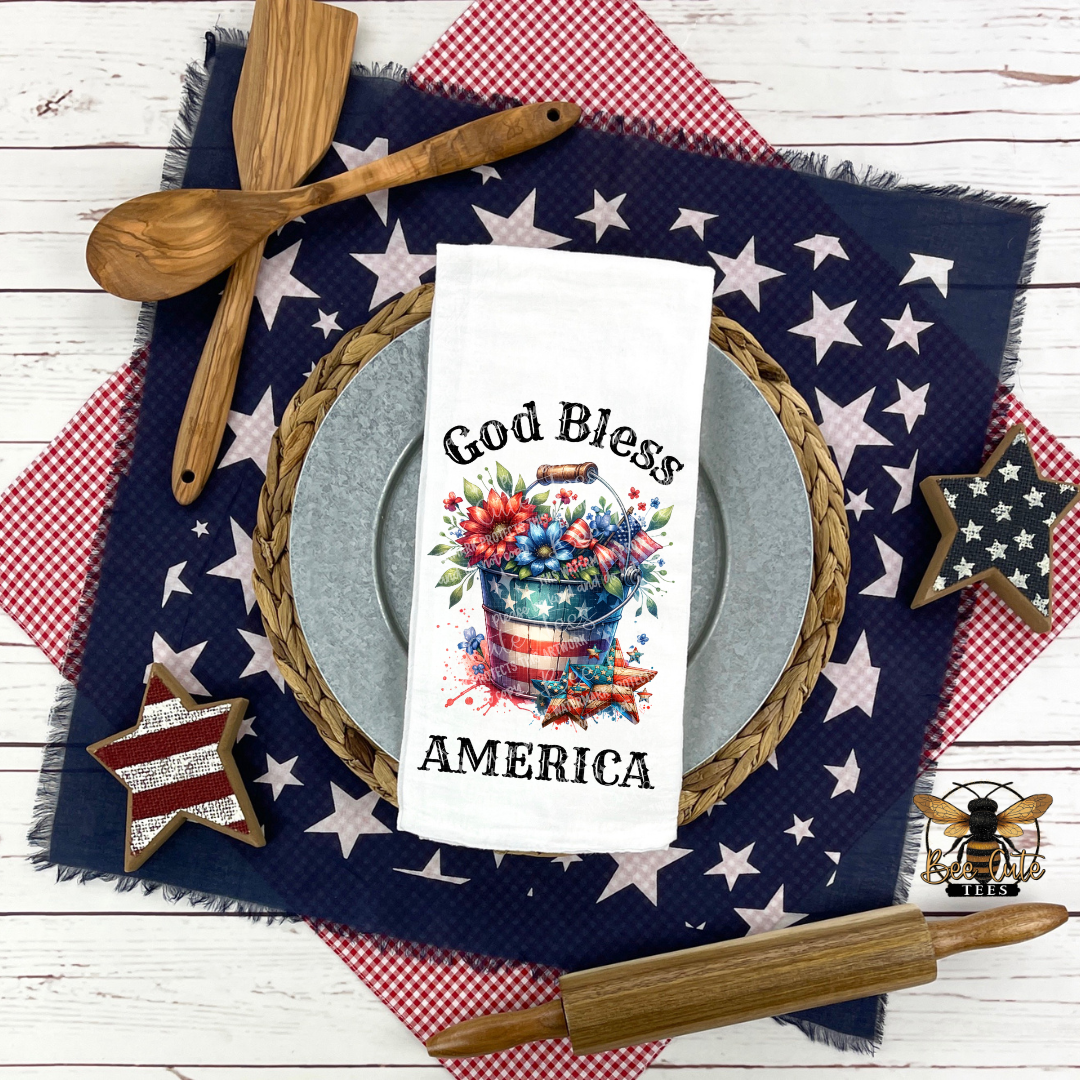 Decorative table setting with 'God Bless America' towel, wooden spoon, and rolling pin on a star-patterned cloth.