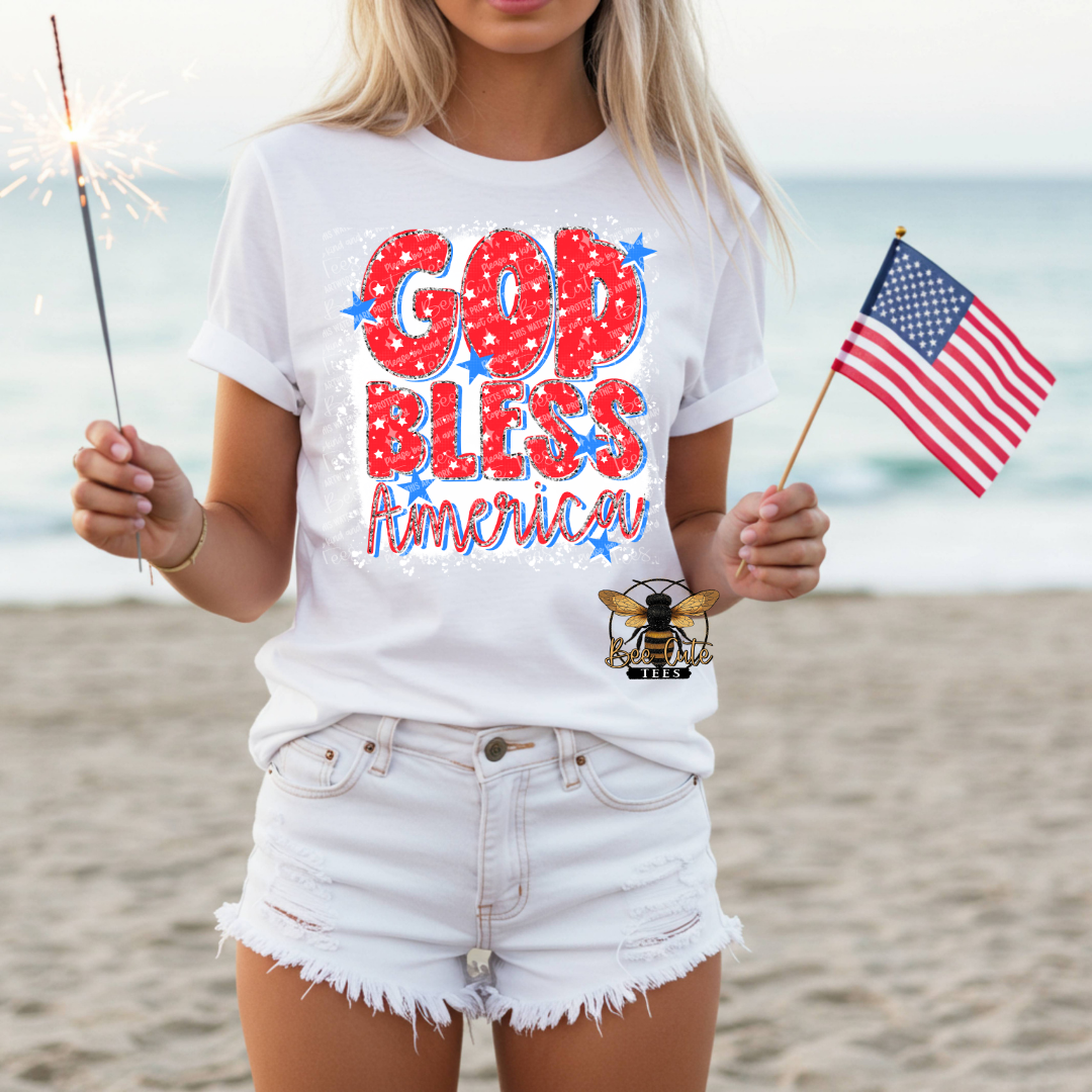 Person wearing a white t-shirt with 'GOD BLESS America' text on a beach