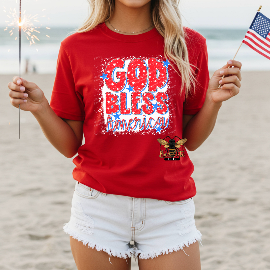 Person wearing a red 'God Bless America' t-shirt on a beach.