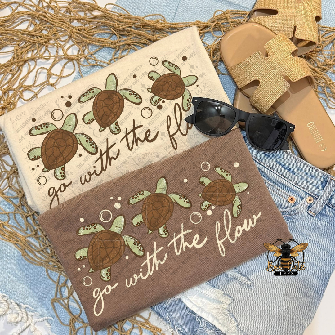 Two beach towels with turtle designs and text, sunglasses, and sandals on a textured surface.