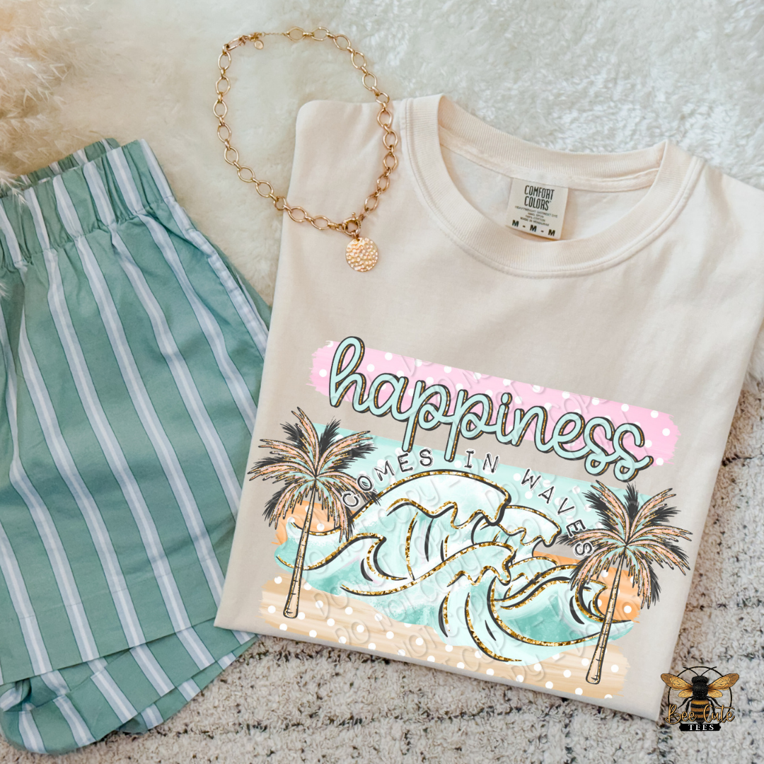 Beige sweatshirt with 'happiness comes in waves' design, green shorts, and gold necklace on a textured surface.
