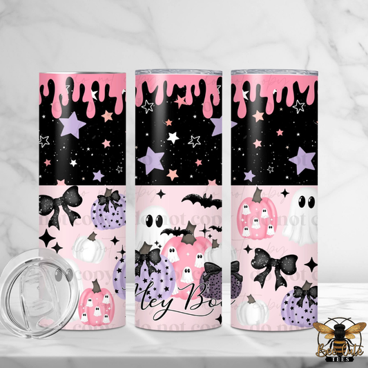 Three slim tumblers with a pink and black Halloween design, featuring stars, bats, ghosts, pumpkins, and purple mushrooms, displayed on a white marble surface with a clear lid in the foreground.