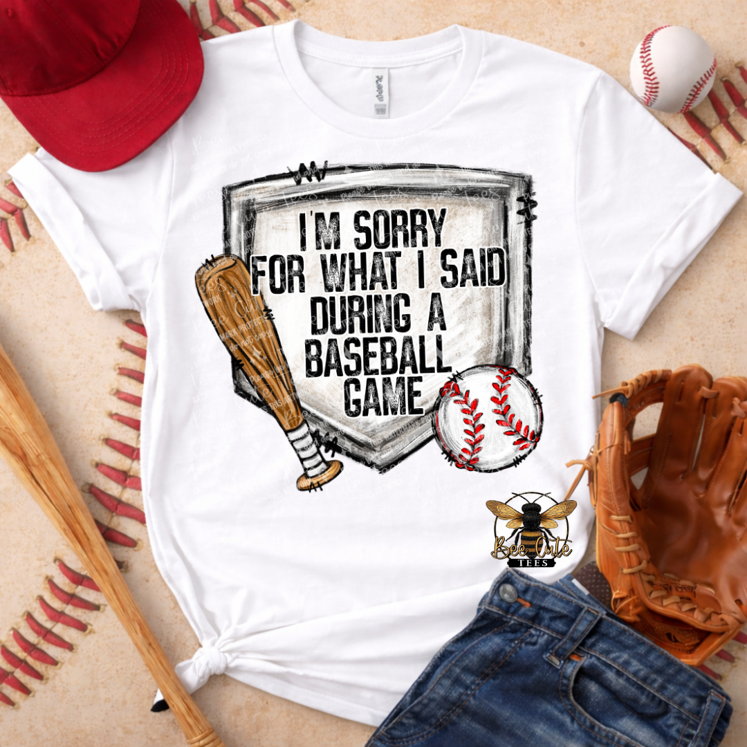 White t-shirt with baseball-themed graphic and text, surrounded by baseball equipment on a wooden surface.